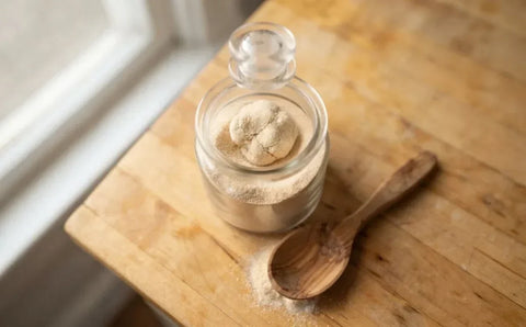 Jar of organic garlic powder with a hardened clump next to a wooden spoon