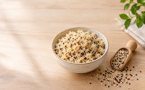 Bowl of cooked quinoa next to raw quinoa seeds on a wooden table