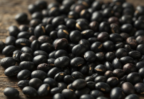 A close-up pile of glossy black beans scattered on a rustic wooden surface.