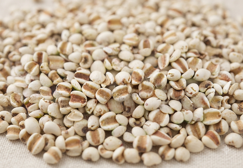 A close-up pile of small oval seeds or grains with off-white bodies and tan to brown stripes, resting on a light beige fabric surface.
