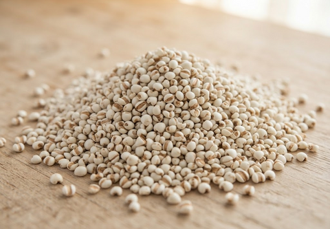 A small mound of beige dried grains or seeds with some darker brown centers, scattered on a light wooden surface.